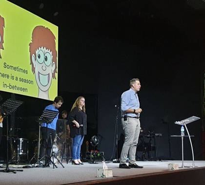 Dave speaking on stage with a cartoon on the big screen